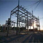 Data center transformer shortage: a high-voltage electrical substation with transformers and switchgear silhouetted at sunset.